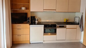 Cocina compacta con armarios de madera, lavavajillas, horno, cafetera y televisor.