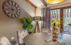 A dining area with a round table, two chairs, a large wall clock, a floor lamp, and a bottle of wine.