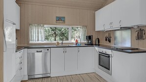 Una cocina compacta con armarios blancos, lavavajillas, estufa y ventana con vista a árboles.