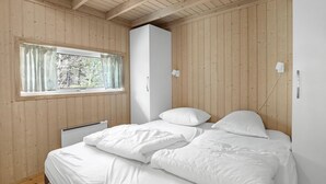 Un dormitorio con techo de madera, cama con ropa de cama blanca, ventana con cortinas y un armario blanco.