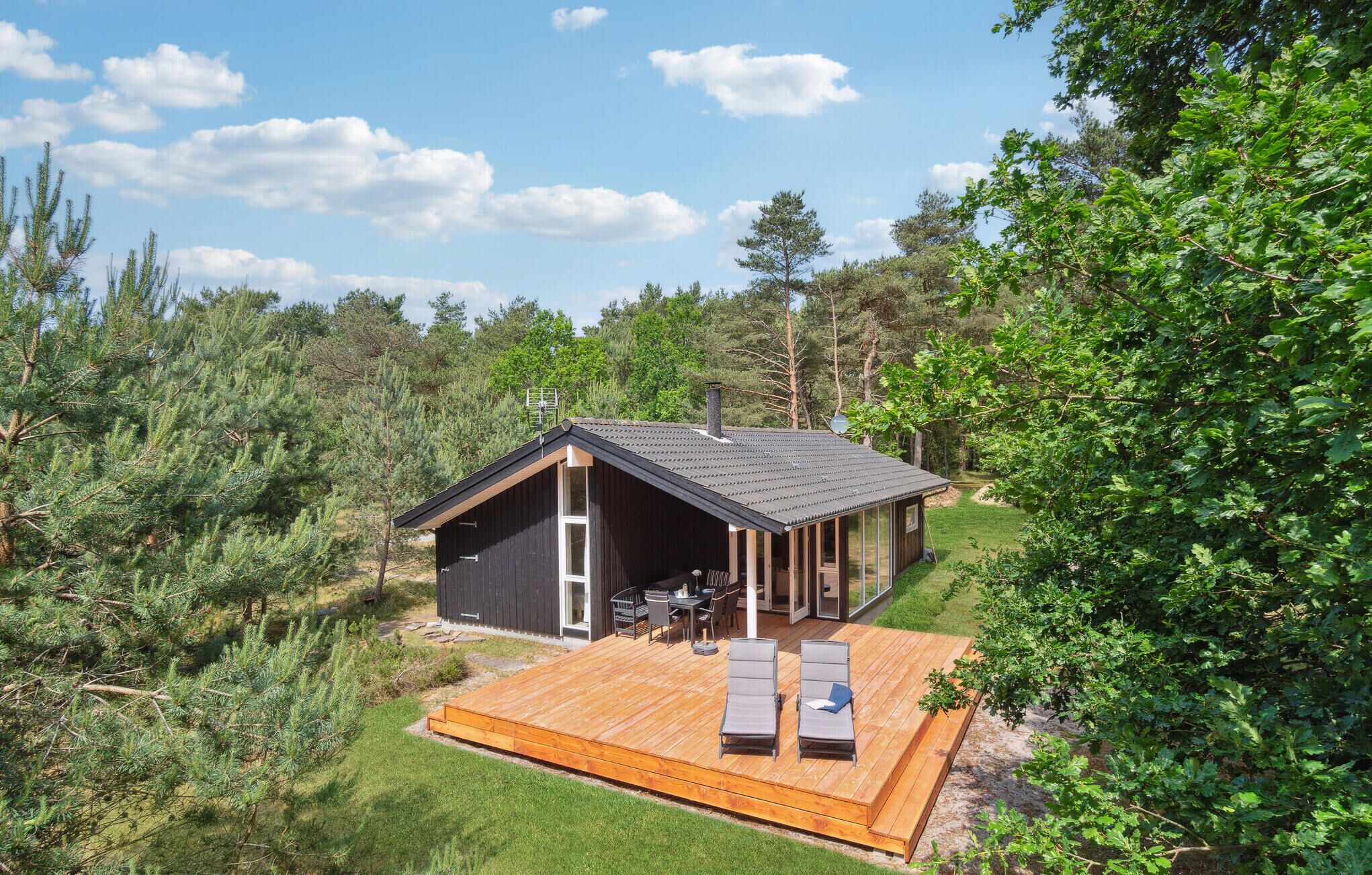 A cabin with a deck, surrounded by trees and a clear sky.
