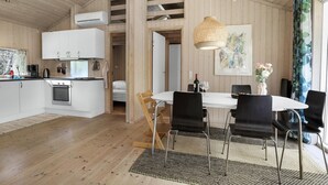 Una cocina moderna con armarios blancos, una estufa y un aire acondicionado. Hay un comedor con una mesa blanca y sillas negras.