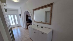 Un couloir avec une coiffeuse blanche, un miroir et un sol carrelé.