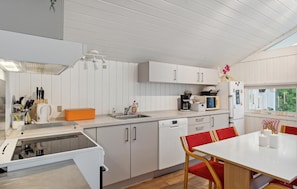 Une cuisine moderne avec des armoires blanches, un four encastré et un coin repas comprenant une table et des chaises.