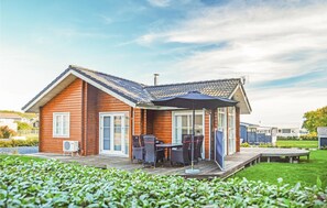 Ein Holzhäuschen mit Ziegeldach, einer überdachten Terrasse mit Gartenmöbeln und einem grünen Garten.
