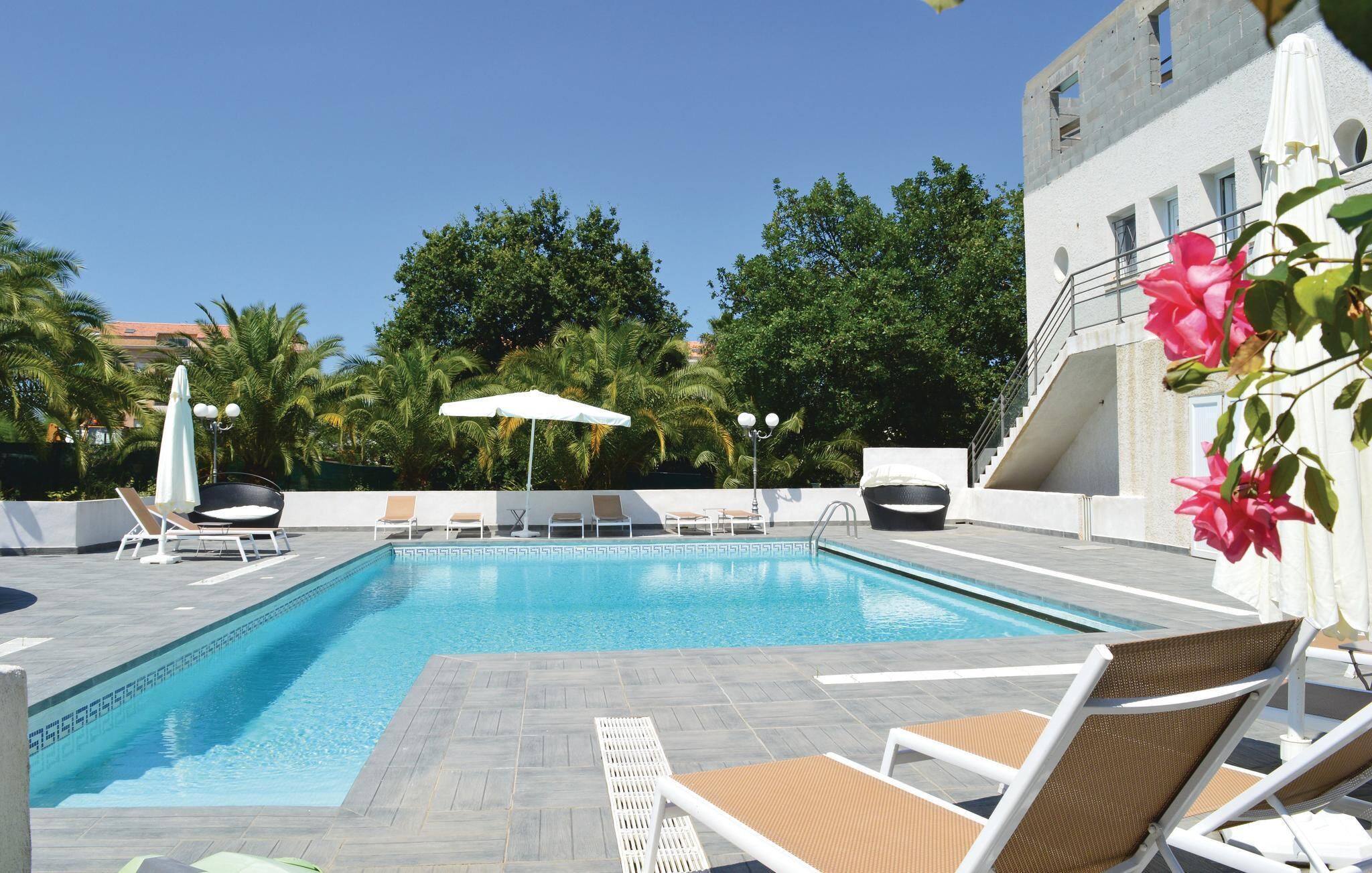 A rectangular swimming pool with a geometric tile pattern, surrounded by lounge chairs and umbrellas.