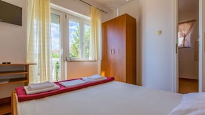 A bedroom with a bed, a wooden wardrobe, a window with curtains, and a small table with towels. - Holiday apartment with balcony (Crikvenica)