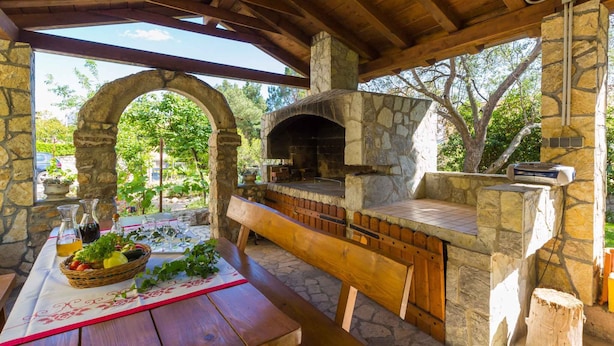An outdoor stone oven with a wooden table and benches, surrounded by stone walls and a covered area. - Holiday apartment with balcony (Crikvenica)