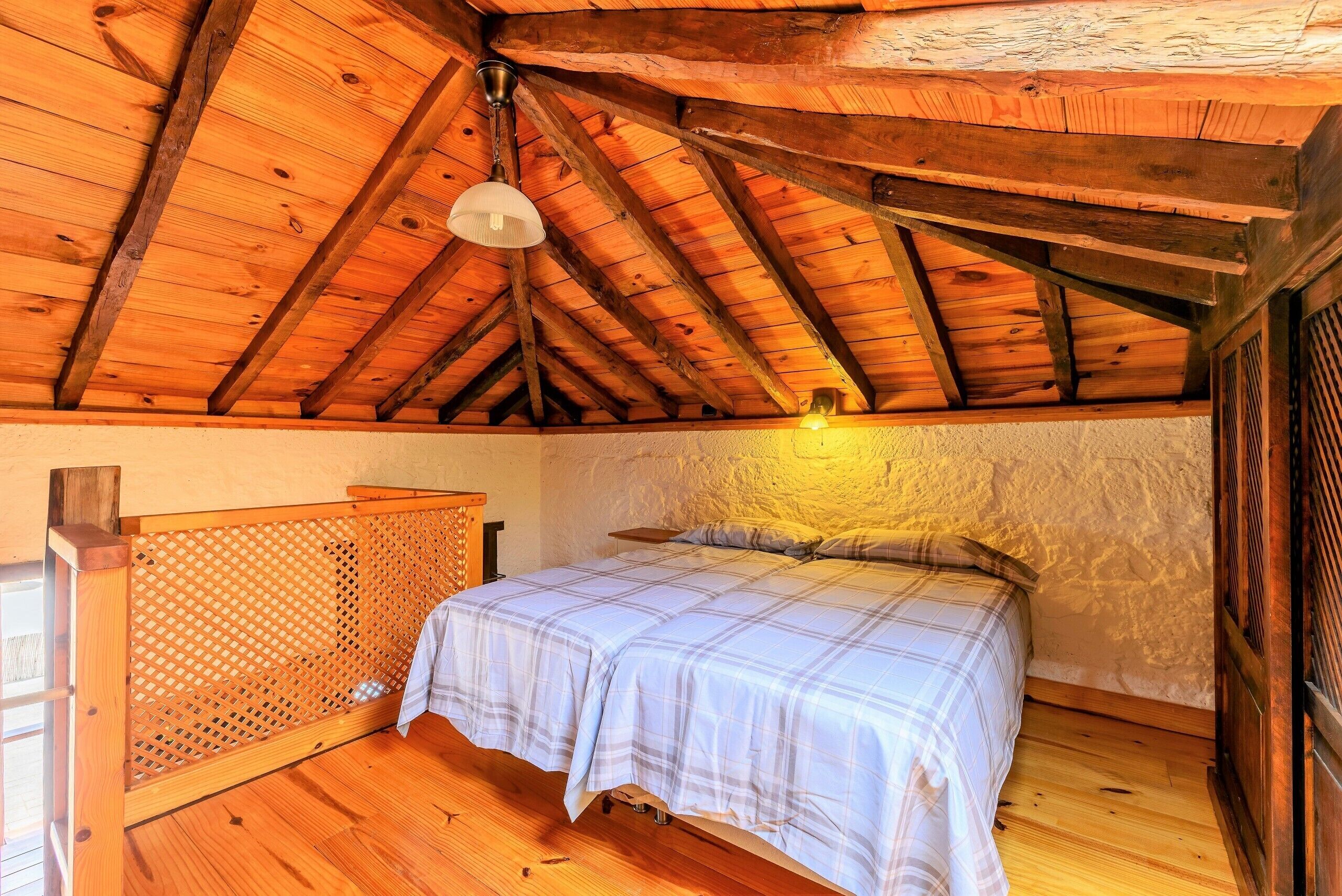A cozy bedroom with a wooden ceiling, a bed with a plaid bedspread, and a wooden headboard.