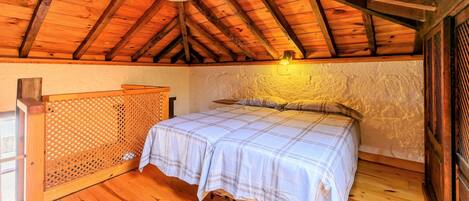 A cozy bedroom with a wooden ceiling, a bed with a plaid bedspread, and a wooden headboard.