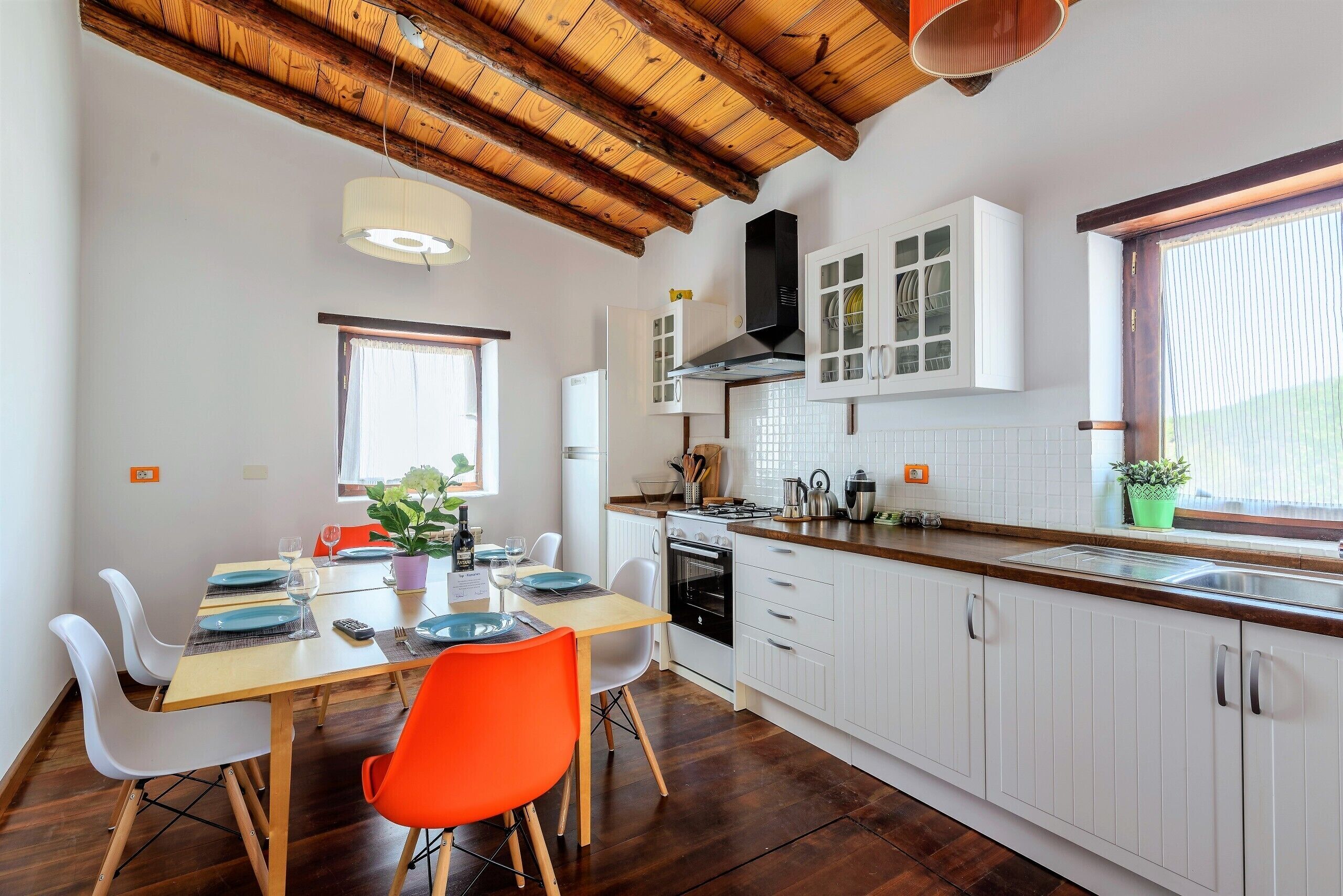 Een moderne keuken met witte kasten, een houten plafond en een eethoek met een tafel voor vier personen.
