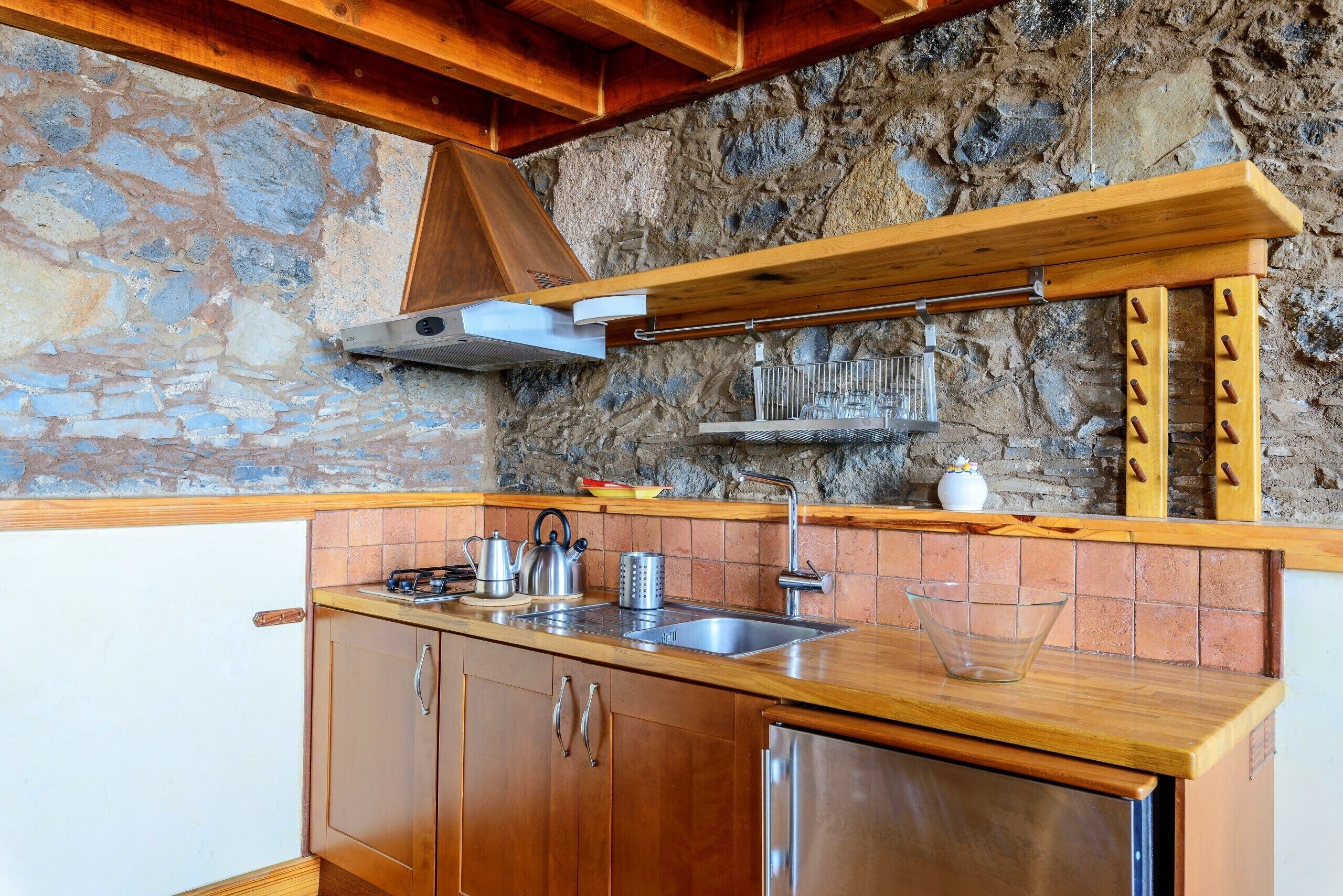 Una cocina con armarios de madera, una pared de piedra y una estufa empotrada.