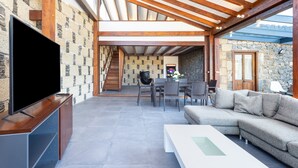An open-plan living area with a TV, sofa, and dining setup. - Casa Rural Altos Cruz de Tea (Granadilla de Abona)