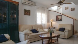 Un salon avec deux canapés beige, une table basse en verre, un ventilateur de plafond et un escalier doté d’une rampe.