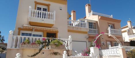 A multi-story building with balconies, a gated entrance, and decorative plants.