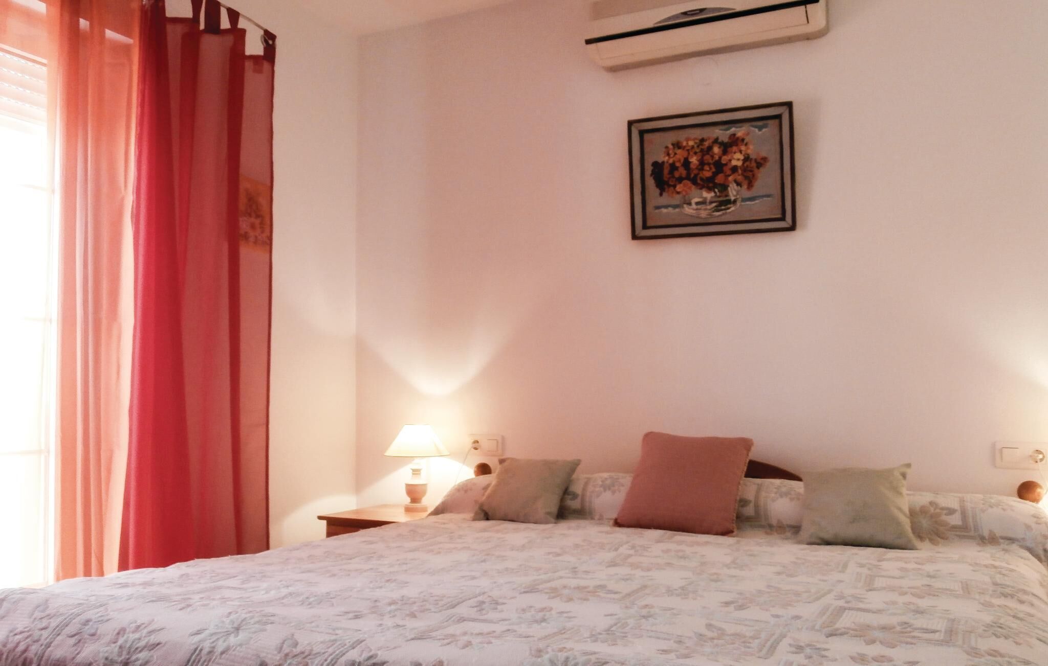 Een slaapkamer met een bed, een nachtkastje, een lamp, een wandairconditioner en een lijst met een foto aan de muur.
