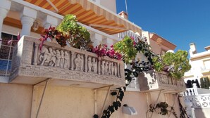 Une façade d’immeuble avec un balcon agrémenté d’une sculpture ornementale en pierre et de plantes en pot.