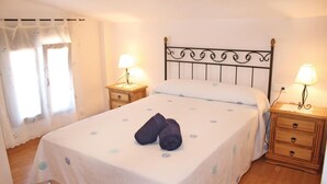 A neatly made bed with a patterned bedspread, two bedside lamps, and a wooden nightstand with drawers. - Lovely home in Frigiliana (Frigiliana)