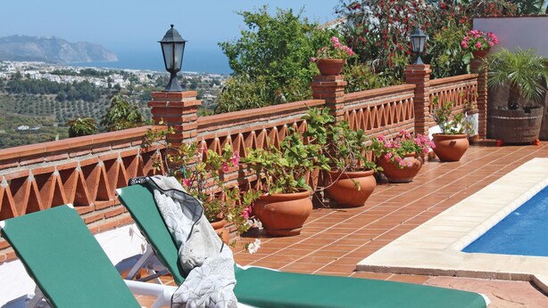 A rooftop terrace with a pool, green lounge chairs, terracotta planters with flowers, and a view of the city and mountains. - Lovely home in Frigiliana (Frigiliana)