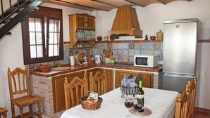 A kitchen with a dining table set for two, a refrigerator, a microwave, and a wooden cabinet with dishes. - Lovely home in Frigiliana (Frigiliana)