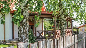 A wooden fence with a pergola structure, a white building with a red roof, and greenery in the background.