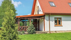 A two-story house with a red-tiled roof, a wooden balcony, and a stone foundation.