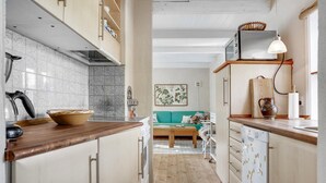 A narrow kitchen with wooden cabinets, a countertop, and a stove. There is a window with a basket on the shelf above it. - 1 bedroom nice home in Knebel (Knebel)