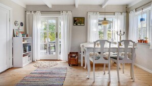 A bright, airy dining room with white furniture, a large window with curtains, and a view of greenery outside. - 1 bedroom nice home in Knebel (Knebel)