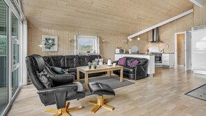 A modern living room with a leather sofa, a wooden coffee table, and a kitchen area with white cabinets and a stainless steel range hood. - Stunning home in Tarm with sauna (Tarm)