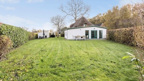 Un bâtiment blanc avec un toit de chaume, un petit patio avec une table et des chaises, et une pelouse bien entretenue.
