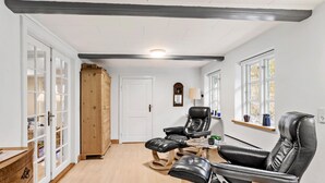 Une pièce avec un meuble en bois, une porte blanche, un fauteuil en cuir noir et une petite table avec une lampe.