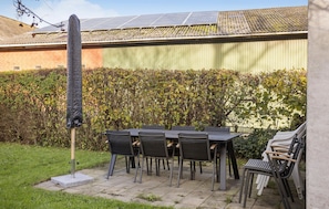 Enjoy dining or socializing in this outdoor patio area with a table and chairs, surrounded by a lush hedge and a building with a green wall.