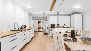 Une cuisine moderne avec des armoires blanches, des comptoirs en bois et un îlot central. On y trouve un coin repas avec une table et des chaises, ainsi qu’une grande fenêtre qui laisse entrer la lumière naturelle.