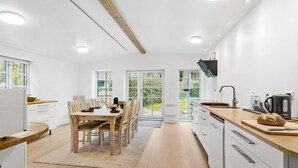 Une cuisine moderne avec des meubles en bois, un coin repas comprenant une table et des chaises, et une vue sur la verdure grâce à de grandes fenêtres.