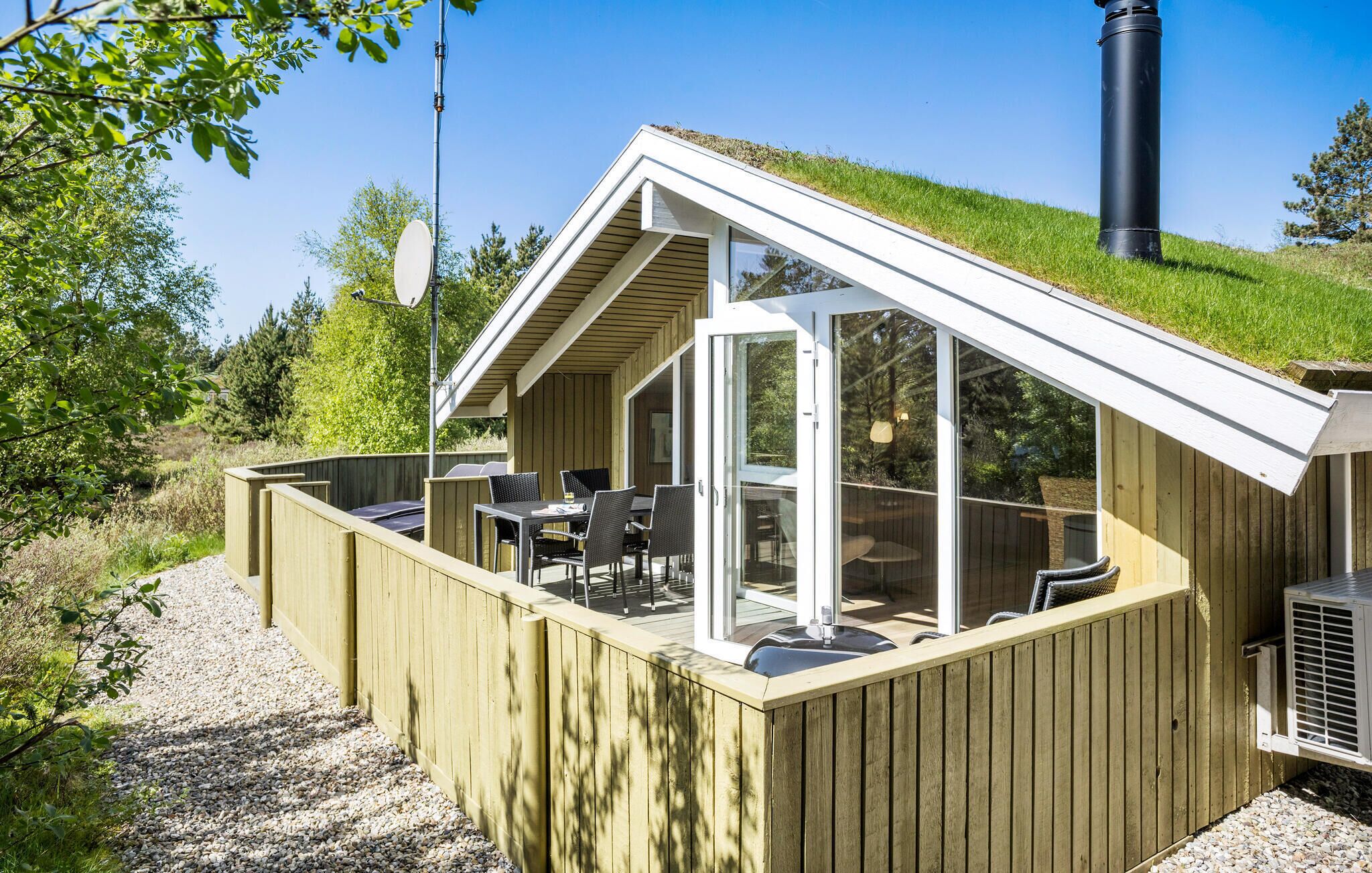 Een houten chalet met een schuin dak, grote glasramen en een grindpad dat naar de ingang leidt.