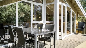 An outdoor patio with a table and chairs, large windows, and a wooden deck. - Beautiful home in Rømø with kitchen (Rømø)