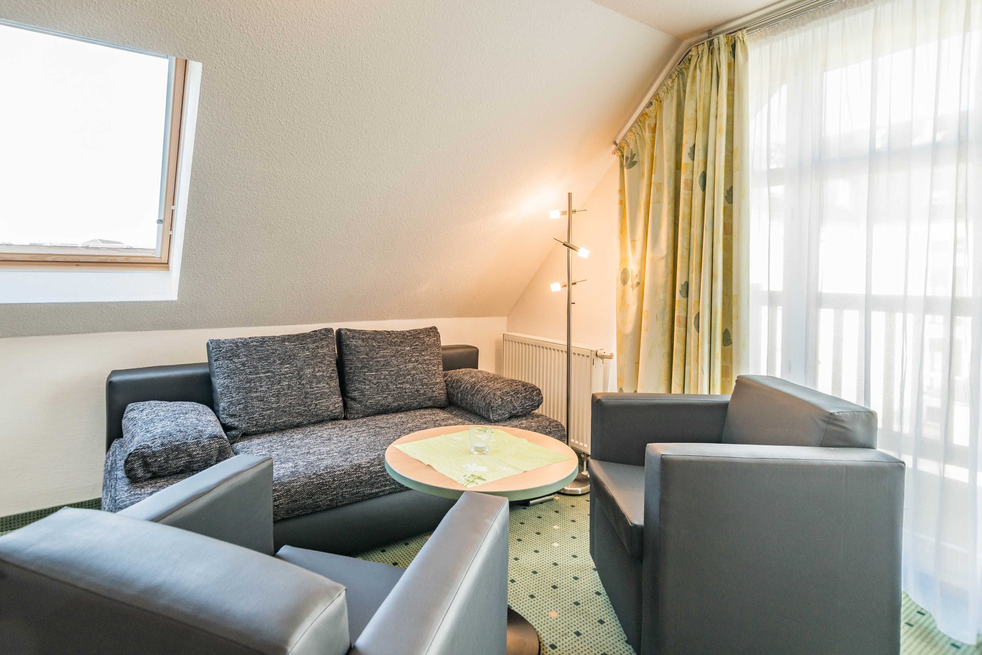 Een moderne woonkamer met een bank, fauteuils, een bijzettafeltje en een vloerlamp.