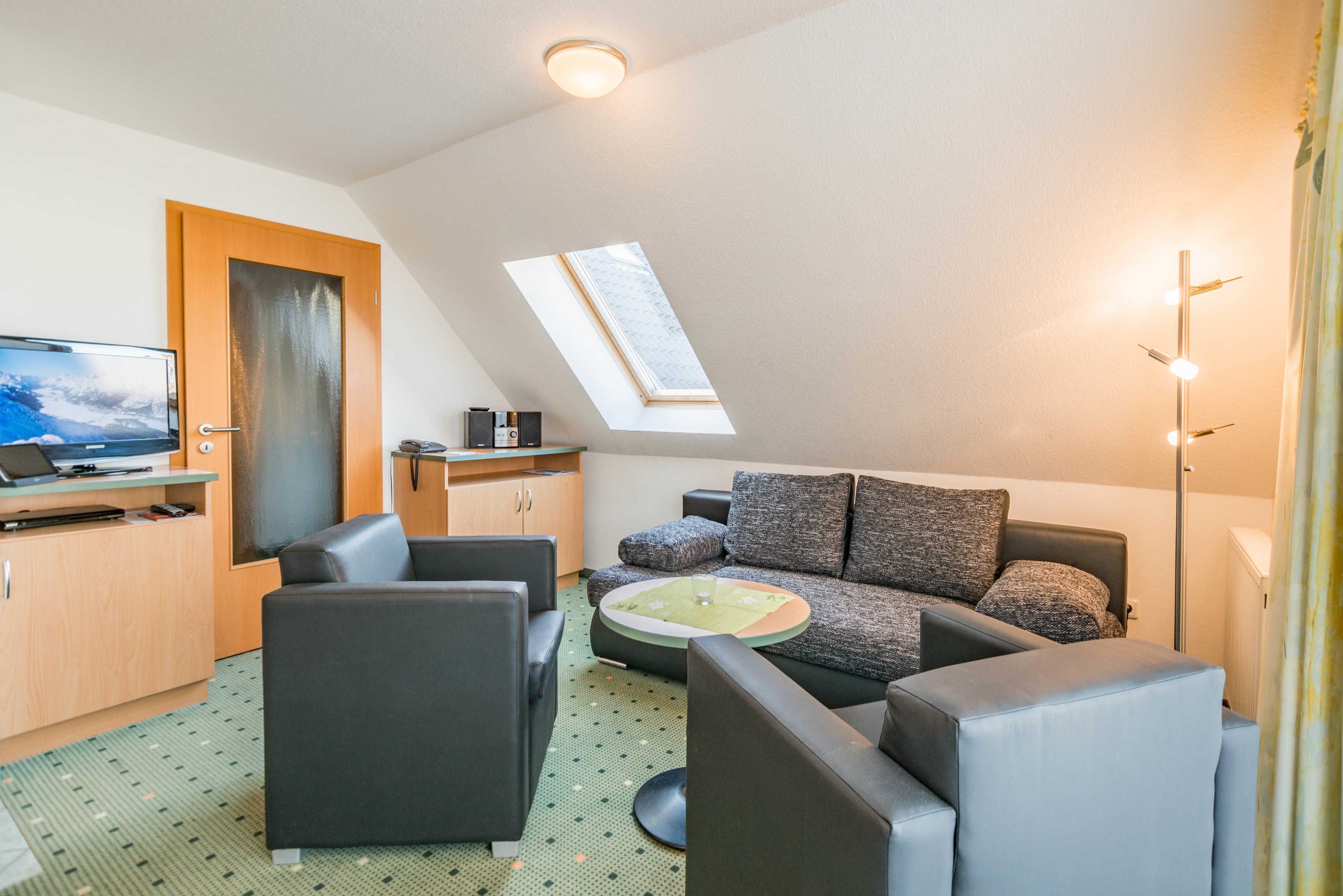 Ein modernes Wohnzimmer mit einer Couch, Sesseln, einem Couchtisch, einem Fernseher und einem Oberlicht.