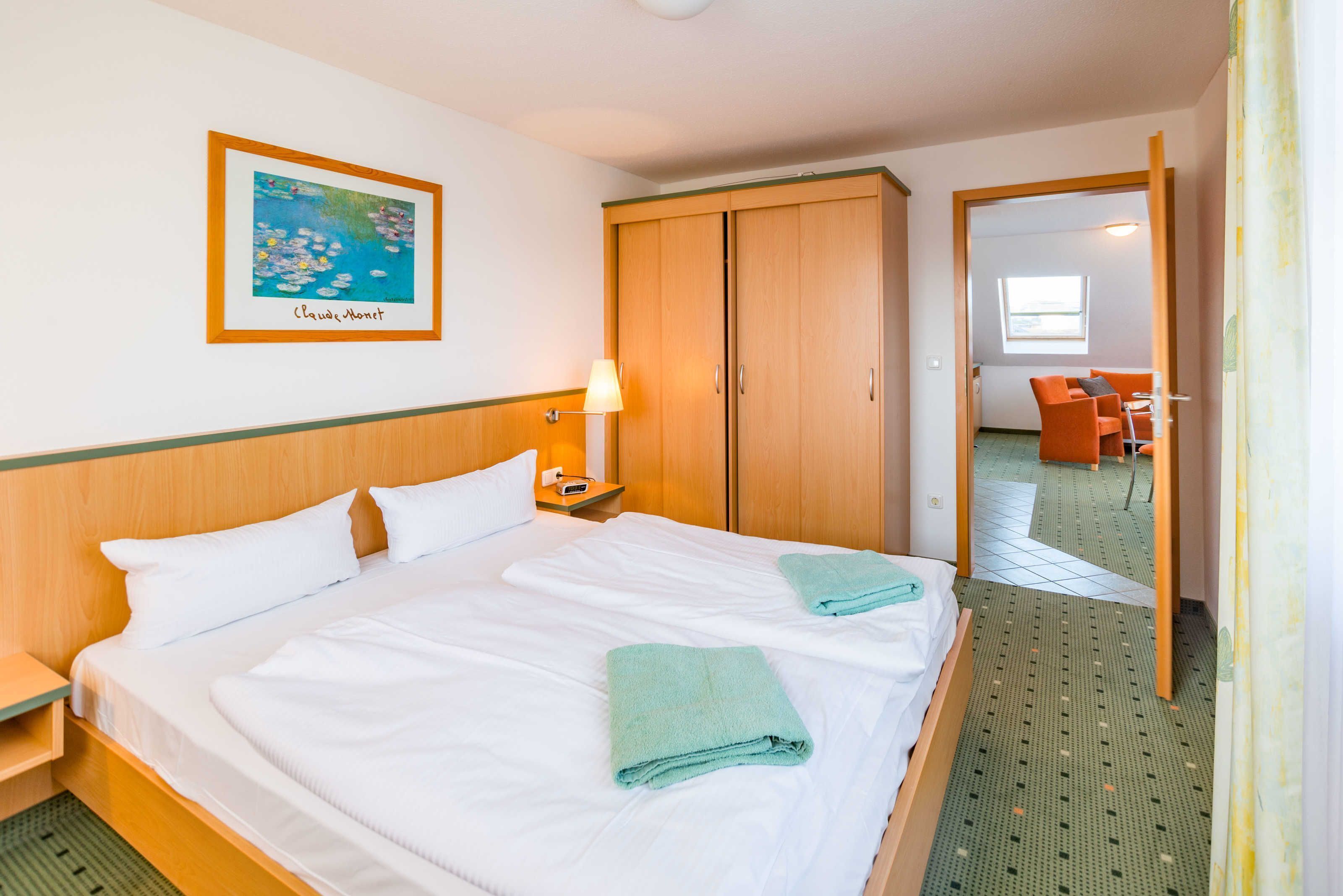 Een hotelkamer met een groot bed, een houten garderobe, een lijst met een schilderij en een spiegel die de kamer weerspiegelt.