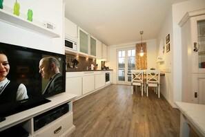 Una cocina moderna con armarios blancos, un comedor con una mesa y sillas blancas, y un televisor sobre un mueble.