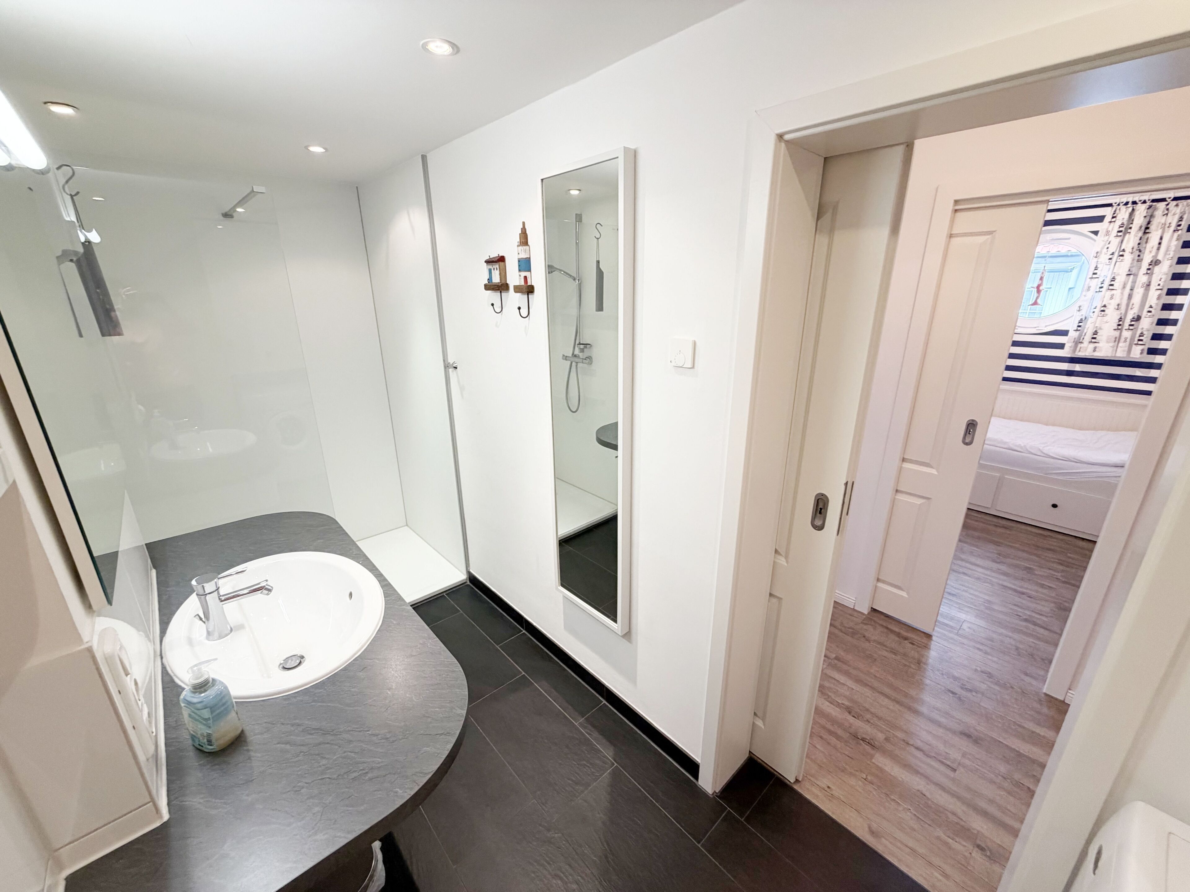 Een moderne badkamer met een gebogen donker aanrecht, een witte wastafel en een douchecabine met glazen wanden.