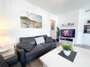 A modern living room with a leather sofa, a flat-screen TV, a coffee table, and a painting of a beach scene.