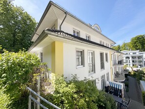 Un immeuble à plusieurs étages, doté d’une façade blanche et de touches de couleur jaune, avec des balcons et un espace extérieur aménagé avec des sièges.