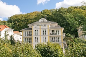 Ein mehrstöckiges Gebäude namens 'Villa Rosa' mit Balkonen und einem Ziegeldach, umgeben von viel Grün.