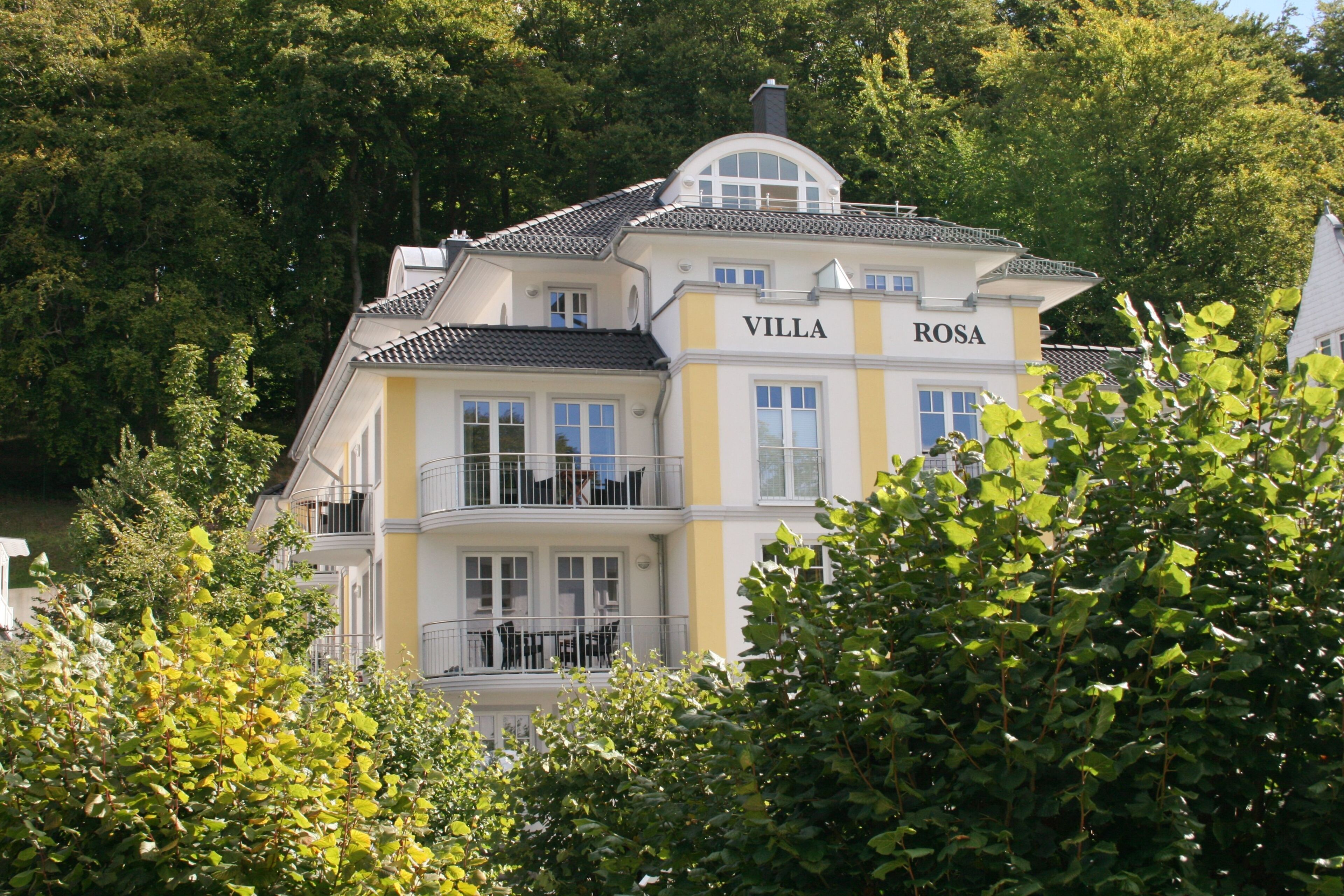 A two-story villa with balconies, surrounded by lush greenery.