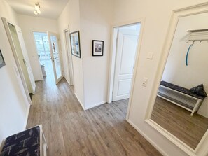A hallway with wooden flooring, white walls, and doors leading to other rooms. There are framed pictures on the walls and a bench with a heater in the corner. - MR: Villa Rosa Whg. 16 Sea magic with 2 roof terraces - Villa Rosa Whg. 16 (Sellin)