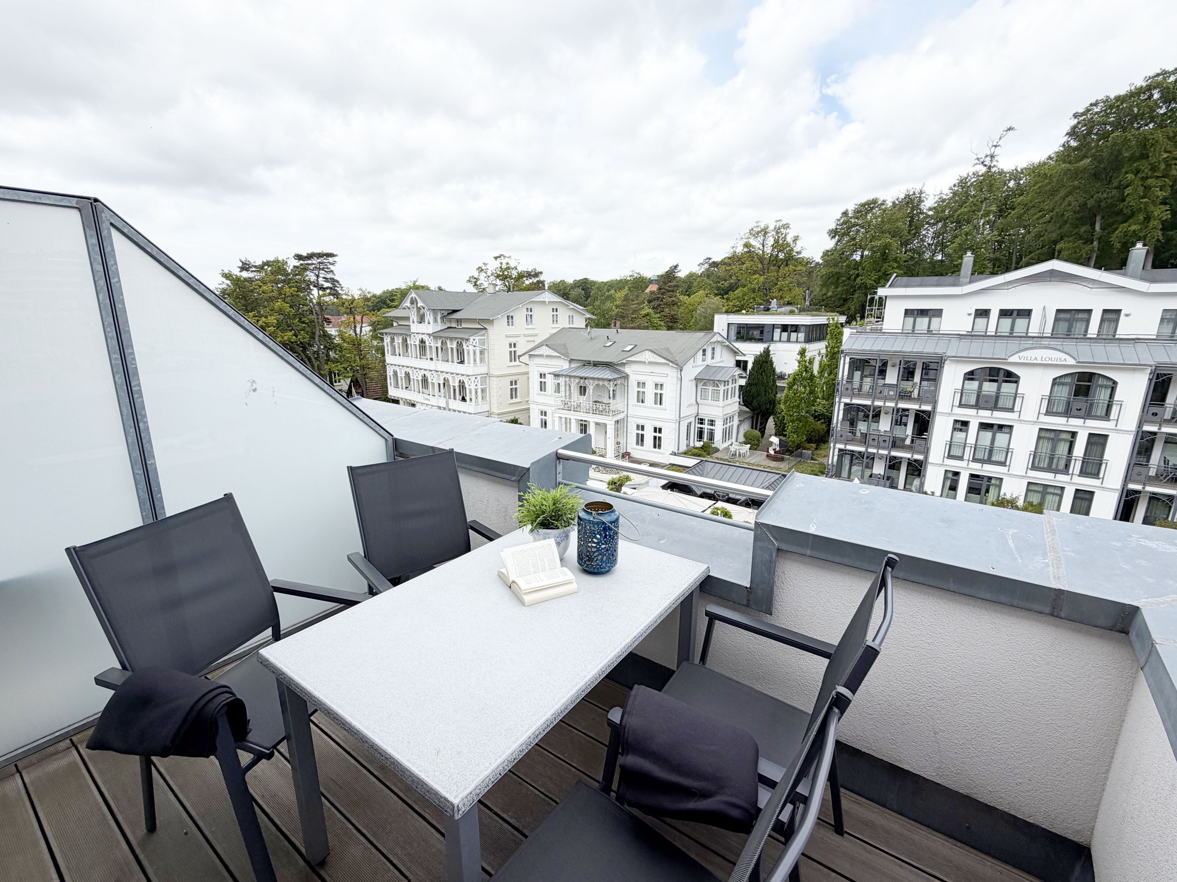 A rooftop terrace with a table and chairs, overlooking a residential area with various buildings.