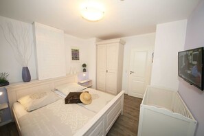 Un dormitorio con cama, armario, mesita de noche, televisor y radiador.