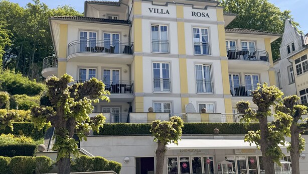A multi-story building named "Villa Rosa" with balconies, a storefront, and well-maintained greenery. - MR: Villa Rosa Whg. 16 Sea magic with 2 roof terraces - Villa Rosa Whg. 16 (Sellin)