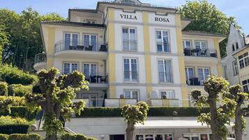 A multi-story building named "Villa Rosa" with balconies, a storefront, and well-maintained greenery.